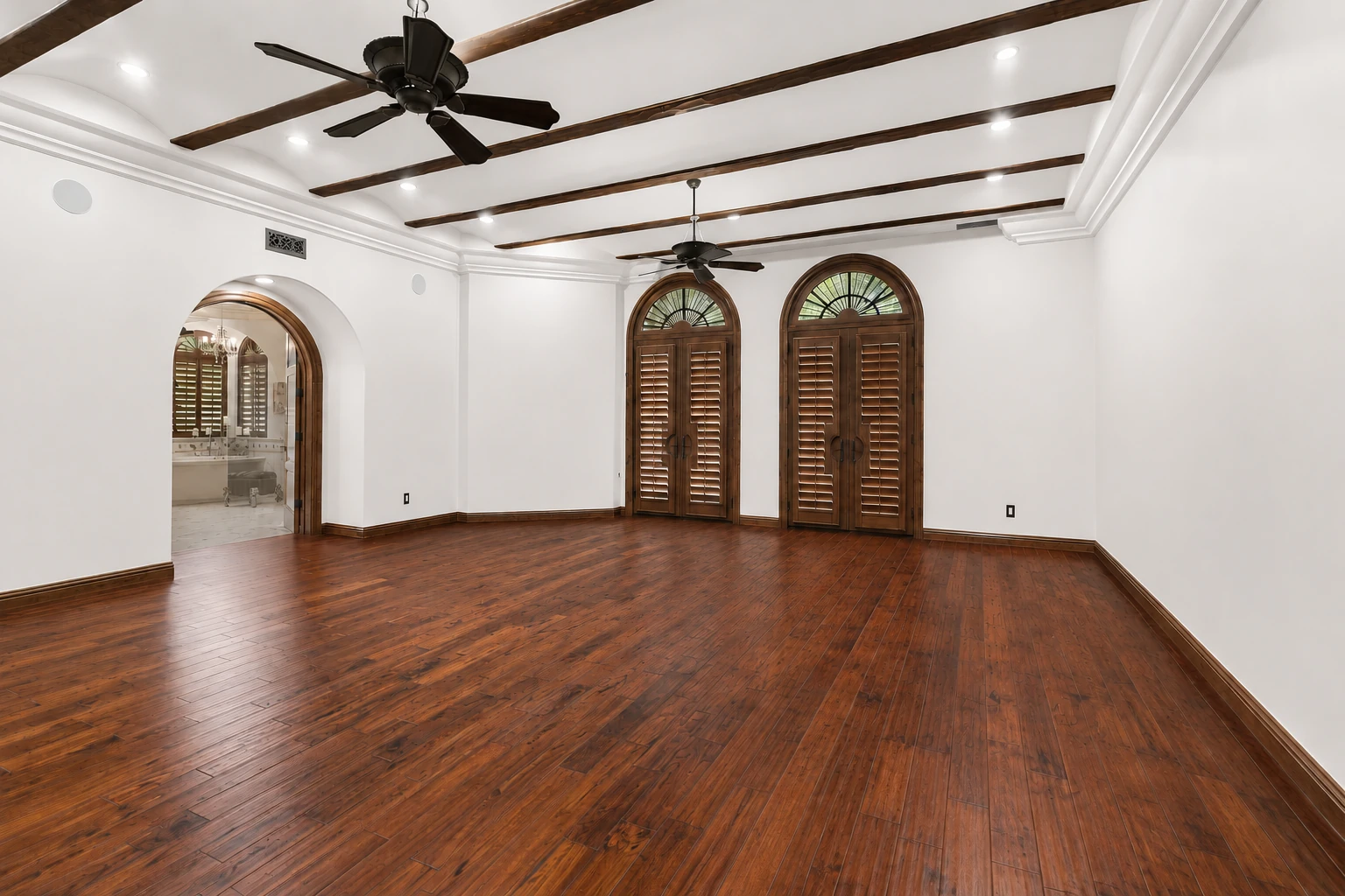 Unfurnished primary suite with wood floors and arched openings