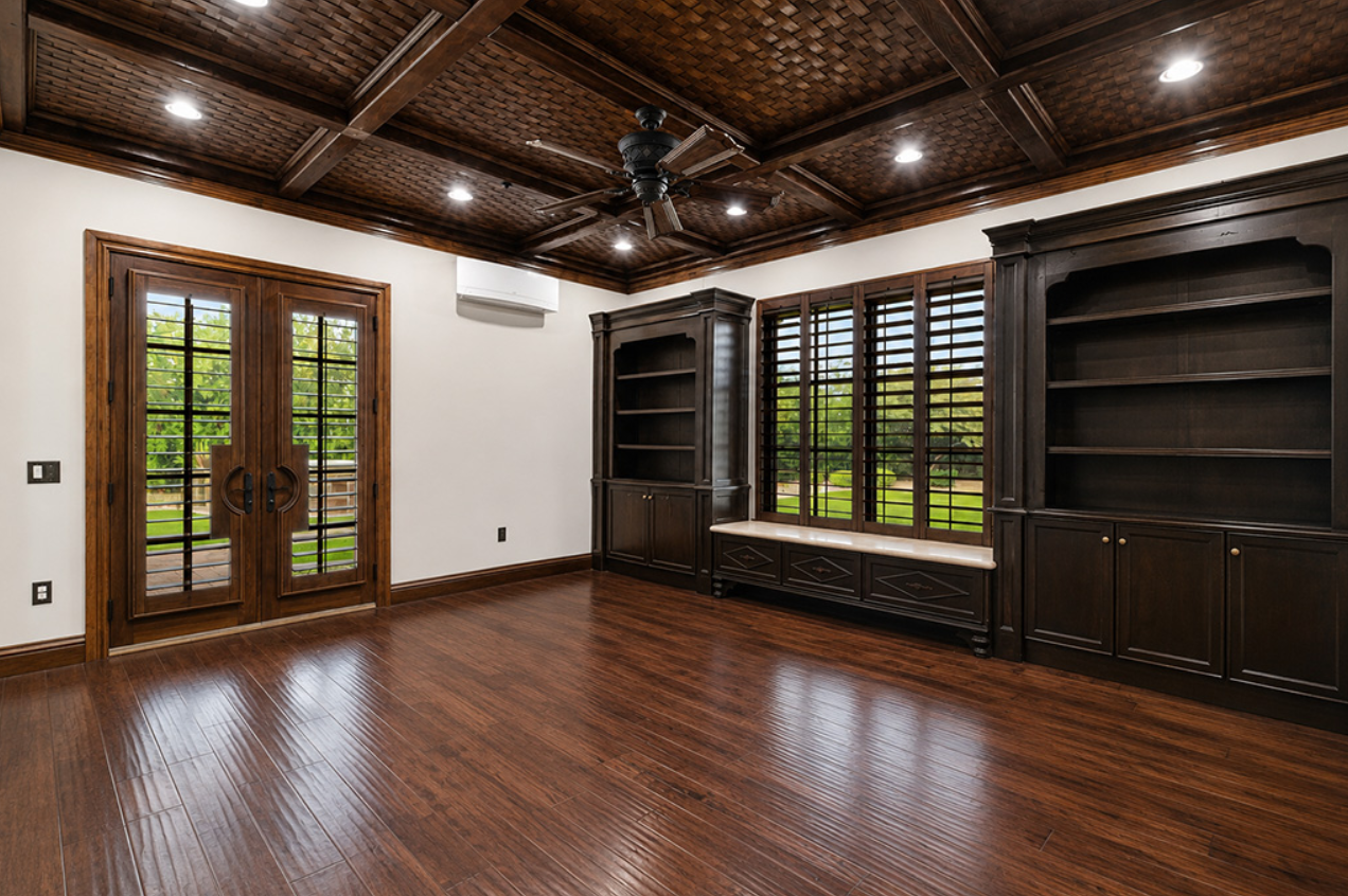Wood-paneled library with built-in cabinetry, shutters, and coffered ceiling